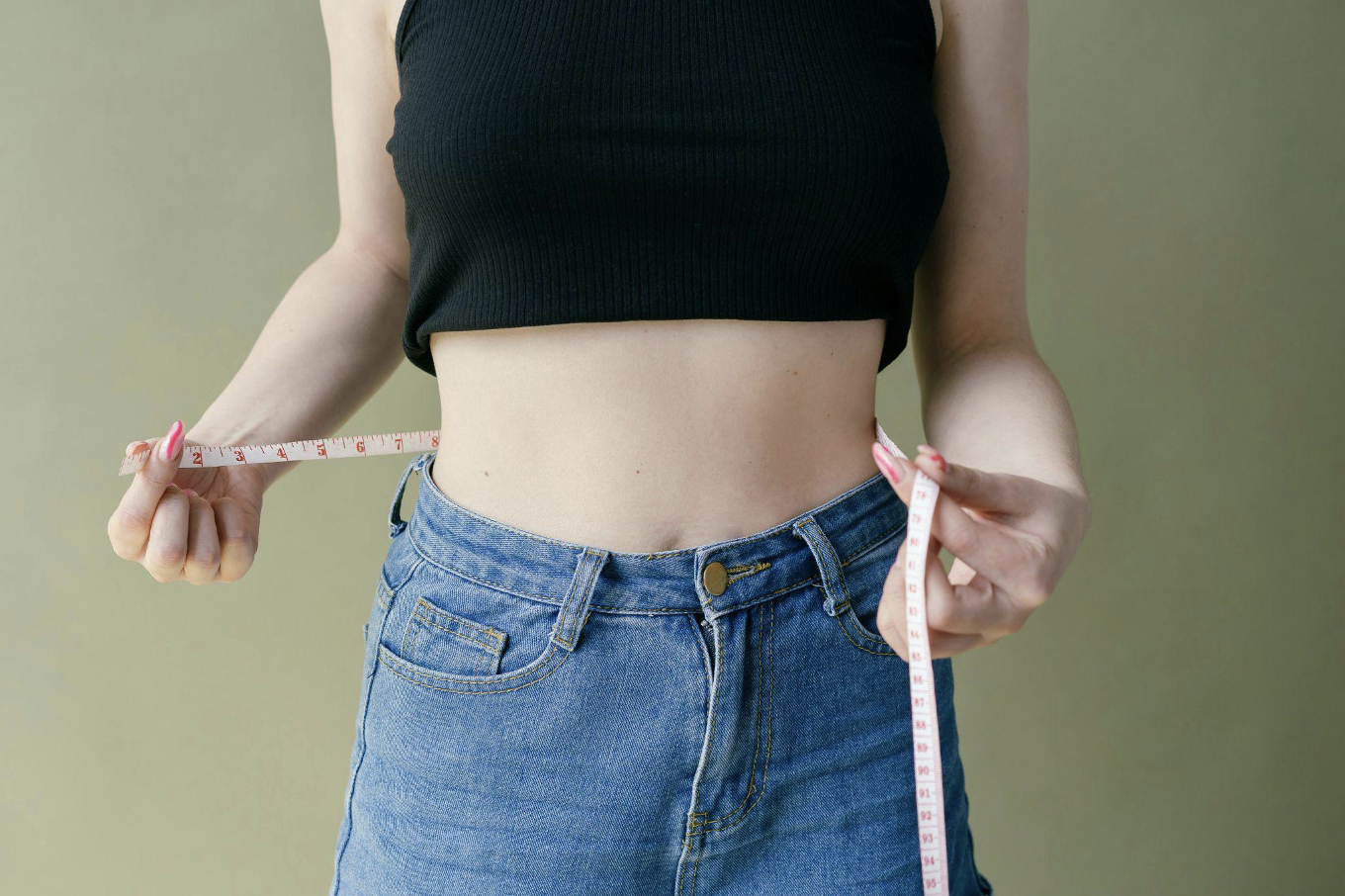 A woman in a crop top measuring her waist