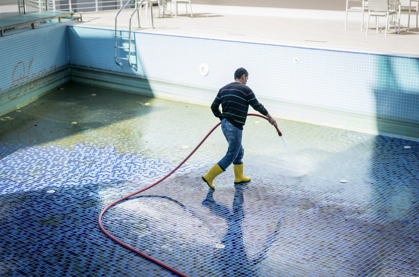 Worker cleaning empty pool with hose